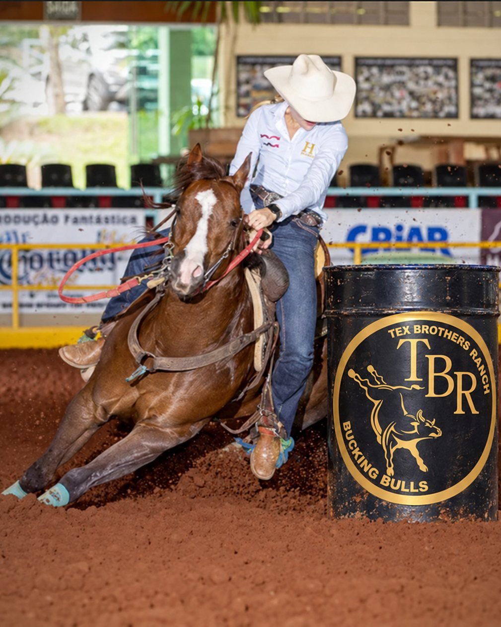 Competidora a cavalo contornando um tambor com a marca Tex Brothers Ranch na prova de 3 tambores